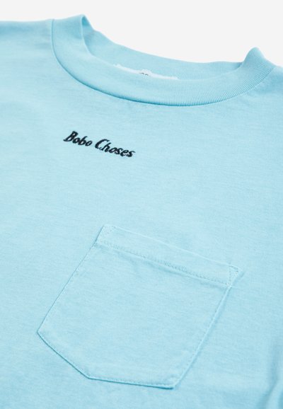 T-shirt in cotone azzurro chiaro con collo rotondo, una piccola tasca sul petto e la scritta "Bobo Choses" ricamata in nero sopra la tasca.