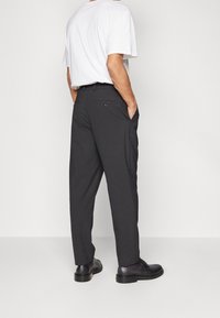 Svarta byxor med en avslappnad passform, med sidofickor och en bakficka med knapppdetailj. Bärs tillsammans med en vit t-shirt och svarta skor.