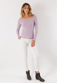 Top lungo a maniche con scollatura tonda di un leggero colore lavanda, abbinato a pantaloni bianchi aderenti e stivaletti neri alla caviglia, che mette in risalto un design minimalista.