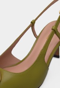 Κοντινή λήψη σε χαμηλό τακούνι δερμάτινου δετήριου παπουτσιού σε ελαιί πράσινο χρώμα με λεπτά λουράκια και μπεζ εσωτερική σόλα.