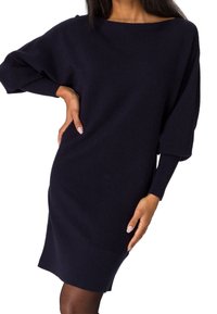 Robe-pull en maille côtelée bleu marine avec large encolure bateau, manches surdimensionnées et poignets côtelés, offrant une coupe décontractée et une longueur mi-cuisse.