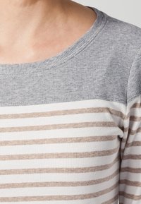 Camicia a maniche lunghe a righe con sezione superiore grigia. La parte inferiore presenta righe orizzontali beige e bianche. Tessuto morbido, scollatura a coste.