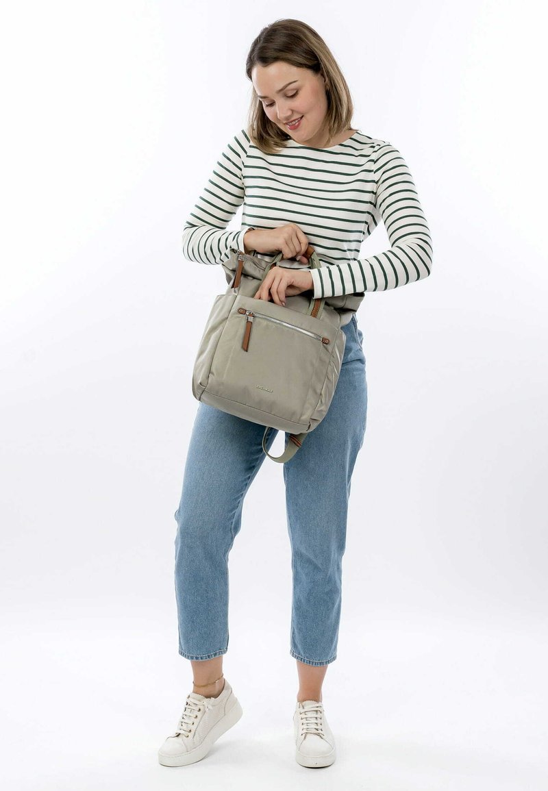 Borsa tote grigia chiara con esterno in tessuto, due manici superiori e tasca frontale con zip. Presenta dettagli in pelle marrone e tracolla regolabile.