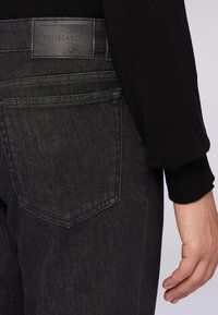 Vaqueros de denim negros con un bolsillo trasero de forma puntiaguda y una etiqueta de cuero con marca en relieve. Textura suave, diseño ajustado.