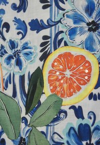 Textília s modrými kvetinovými vzormi, zelenými listami a nakrájaným pomarančom na svetlom pozadí pre výrazný kontrast.