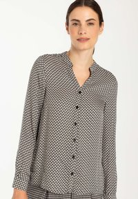 Schwarz-weiße gemusterte Bluse mit V-Ausschnitt, langen Ärmeln und Knopfleiste. Leichter Stoff mit geometrischem Design.