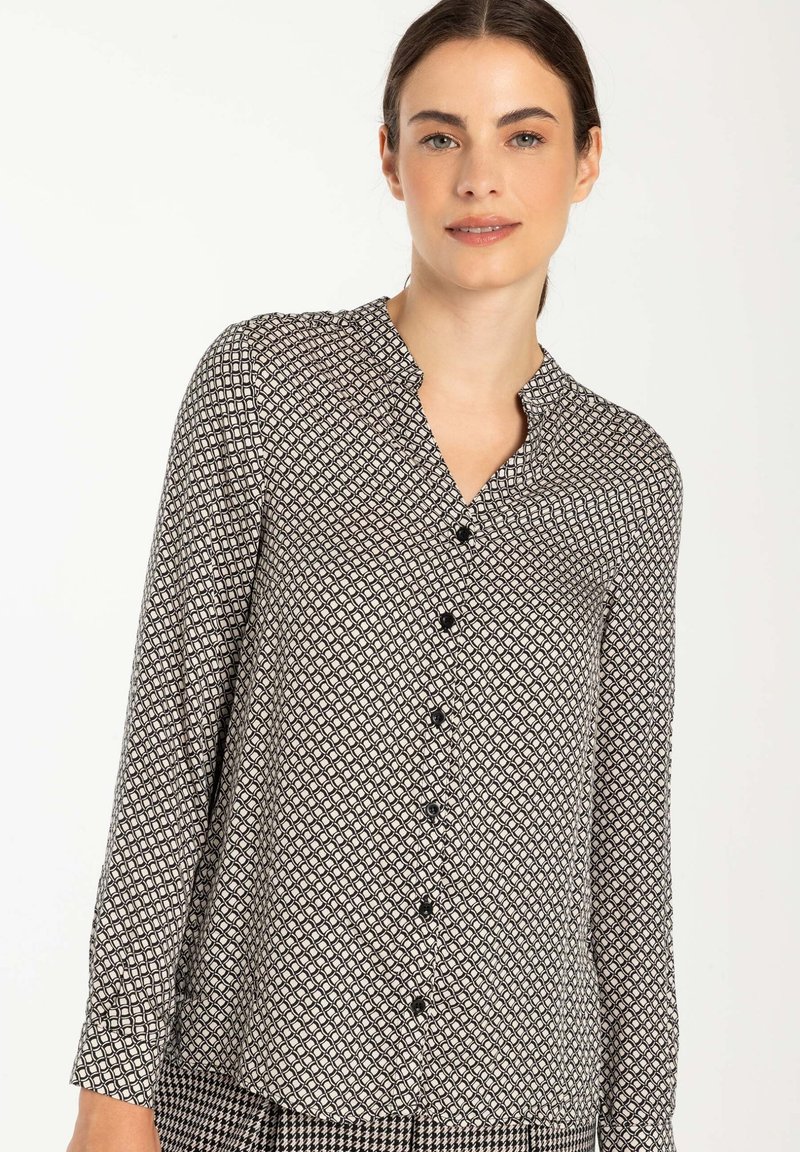Schwarz-weiße gemusterte Bluse mit V-Ausschnitt, langen Ärmeln und Knopfleiste. Leichter Stoff mit geometrischem Design.