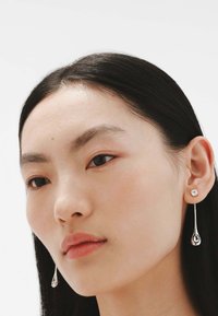 Pendientes de plata en forma de lágrima con un acento de cristal. Acabado suave con una superficie reflectante.