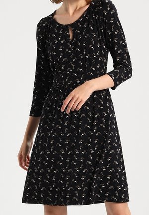 Musta polvipituinen mekko, jossa on 3/4-hihat ja pieni valkoinen lintukuosi. Mekossa on pyöreä pääntie ja avainreikäyksityiskohta.