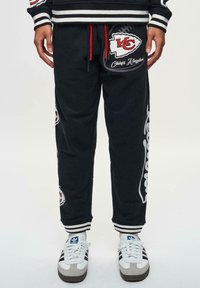 Mörka sweatpants med röd dragsko, med Kansas City Chiefs-logotyper, vita accenter och randiga muddar. Mjuk tygkvalitet med avslappnad passform.