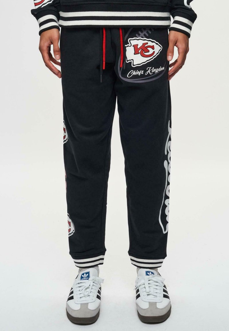 Mörka sweatpants med röd dragsko, med Kansas City Chiefs-logotyper, vita accenter och randiga muddar. Mjuk tygkvalitet med avslappnad passform.