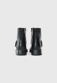 Bottines en cuir noir avec une texture lisse, fermeture éclair à l'arrière, design minimaliste et talon carré. Présente un accent décoratif en métal.