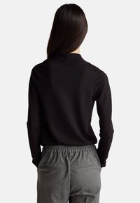 Czarny, długi rękaw top z kołnierzem typu mock, zestawiony z szarymi, luźnymi spodniami z elastycznym pasem, posiadającymi tylne kieszenie.
