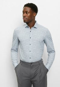 Hellblaues Paisley-Hemd mit langen Ärmeln, knöpfbarem Kragen und glattem Stoff; kombiniert mit grauen Anzughosen.