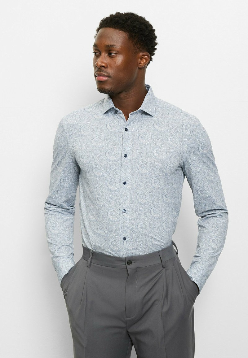 Hellblaues Paisley-Hemd mit langen Ärmeln, knöpfbarem Kragen und glattem Stoff; kombiniert mit grauen Anzughosen.