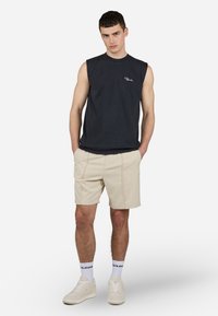 Sort ærmeløs t-shirt, beige shorts med synlige sømme, hvide sneakers og hvide sokker med sort skrift. Simpel, afslappet pasform.