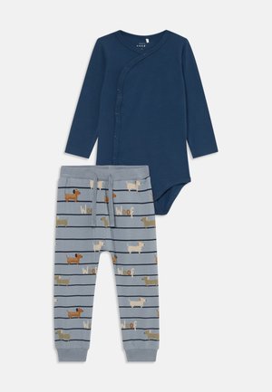 Navy blue long-sleeve baby bodysuit with snap buttons paired with light blue pants featuring dog illustrations and "Woof" text.