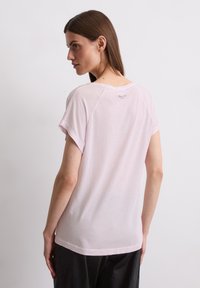 Lichtroze t-shirt met korte mouwen, ronde hals, zachte textuur en subtiele branding op de achterkant. Eenvoudig ontwerp, ontspannen pasvorm.