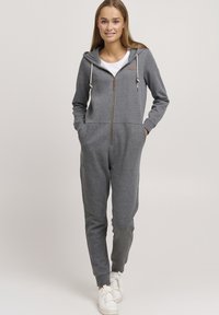 Salopette in cotone grigio misto con zip anteriore, cappuccio, tasche laterali e dettagli con cordino. Polsini a coste e vestibilità morbida.