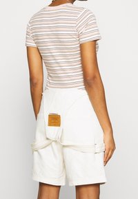 Krátký pruhovaný triko v růžové a bílé barvě s kulatým výstřihem, spárované s bílými bavlněnými šortkami s zadní nášivkou a kapsami na nářadí.