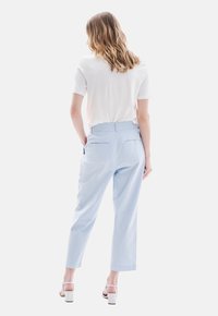 Pantalones de color azul claro con corte recto, que cuentan con bolsillos traseros, combinados con una blusa blanca de manga corta. Textura de tela suave.