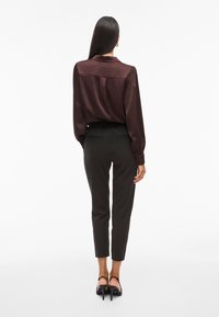 Temno burgundijska satenasta bluzica s napihnjenimi rokavi, v kombinaciji s tesnimi črnimi hlačami. Manekenka nosi črne sandale s peto.