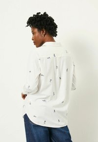 White shirt with small, colorful pattern of nautical elements, collared design, long sleeves, and a curved hem. Made of lightweight fabric.