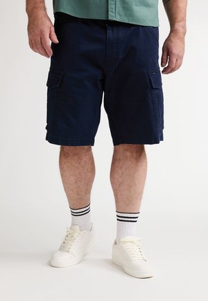 Marineblauwe cargoshorts met zijzakken, gemaakt van een stof met een gladde textuur. Gecombineerd met witte sneakers en geribde sokken met zwarte strepen.