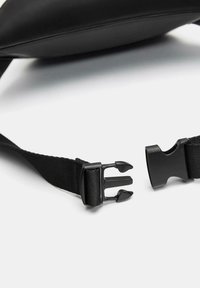 Czarna zapięcie na klamrę z regulowanym nylonowym paskiem. Gładkie skórkowe ciało, minimalistyczny design. Widoczny bezpieczny mechanizm zapięcia.