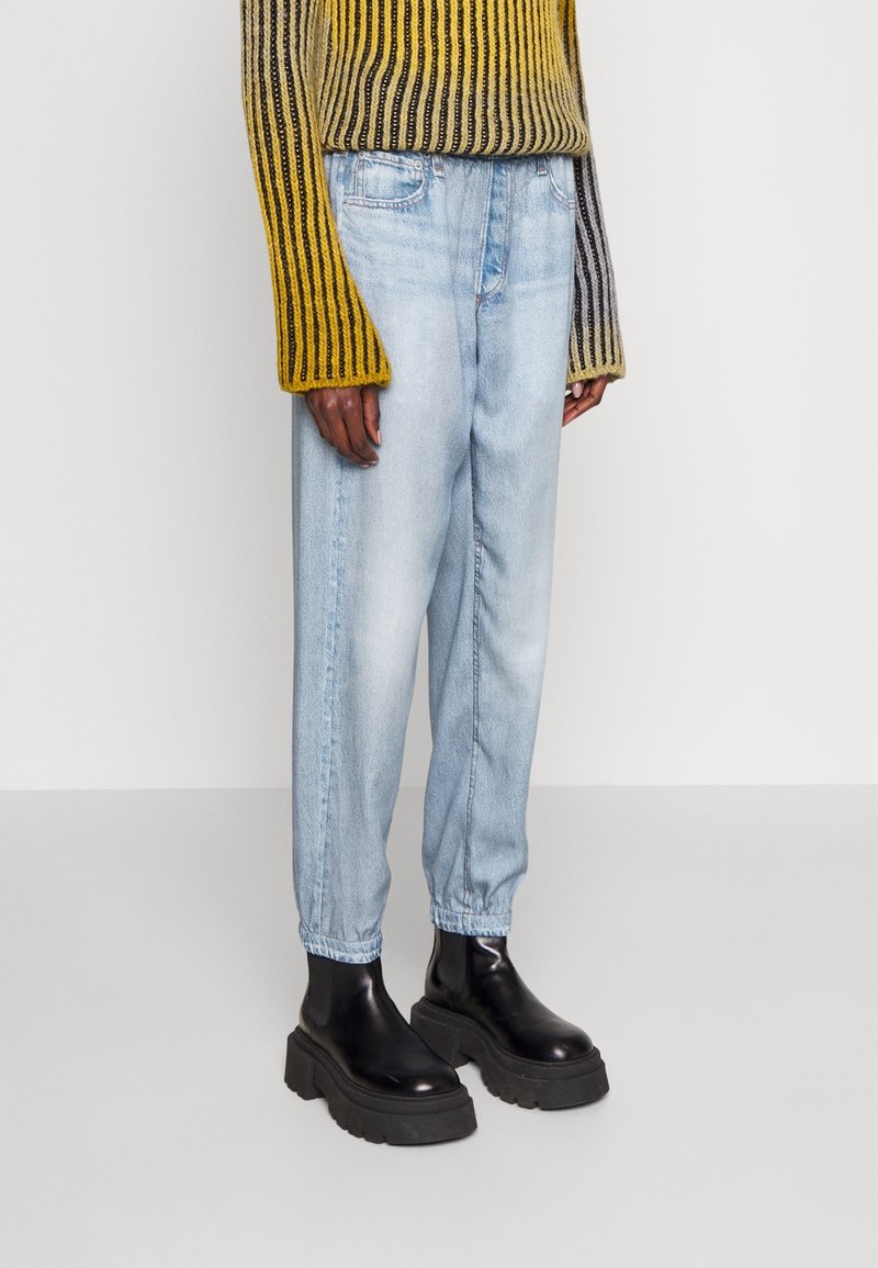 Lysblå denimjeans med en afslappet pasform, elastiske manchetter og sidelommer, parret med en stribet oversized sweater i gul og grå samt sorte støvler.