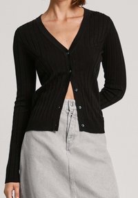 Černý žebrovaný cardigan s výstřihem do V, zdobený modrými knoflíky a dlouhými rukávy. Stylizovaný s světle šedou sukní.