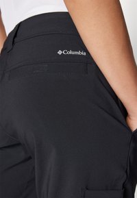 Juodosios Columbia firmos cargo kelnės pasižymi lygiu paviršiumi, elastingu juosmeniu, užpakalinėmis kišenėmis ir logotipo detale viršutiniame dešiniajame šone.