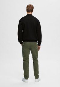 Zwarte sweatshirt met een kraag, gecombineerd met olijfgroene broek. De outfit heeft een relaxte pasvorm en witte sneakers. Achteraanzicht.