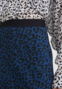 Blue leopard print skirt with a black waistband, paired with a semi-transparent blouse featuring a similar black and white animal pattern.