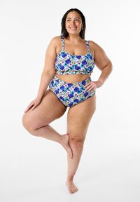 Maillot de bain deux pièces à imprimé floral en violet, jaune et vert. Le haut a des bretelles larges et un décolleté carré ; le bas est taille haute avec des découpes.