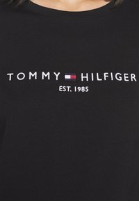 T-shirt nera in cotone con logo ricamato "TOMMY HILFIGER" con accenti blu, rossi e bianchi; anno di fondazione 1985 sotto il logo.