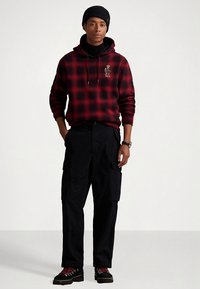 Κόκκινο και μαύρο καρό hoodie με κορδόνια, σε συνδυασμό με μαύρο cargo παντελόνι. Το σύνολο περιλαμβάνει βαριά μαύρα μποτάκια με κόκκινα κορδόνια.