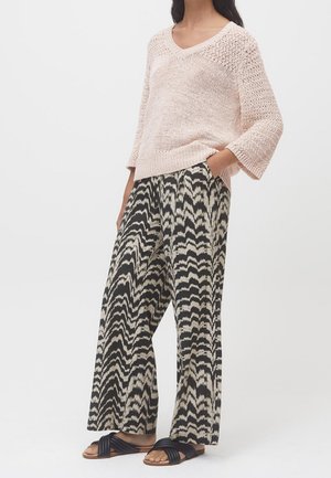 Un pull en tricot rose clair avec un col en V. Un pantalon large noir et beige avec un motif en zigzag. Des sandales noires avec des brides tordues.