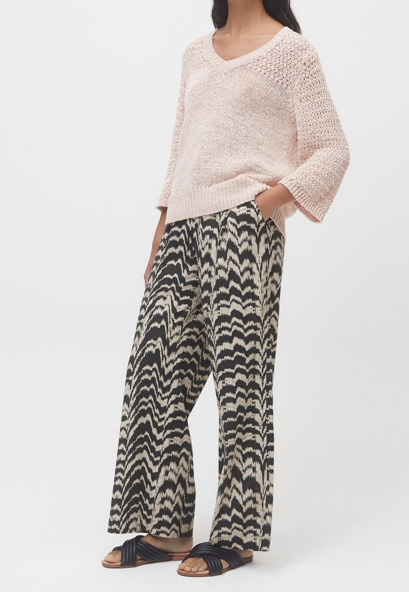 Jasnoróżowy, dziany sweter z dekoltem w serek. Czarno-beżowe szerokie spodnie z wzorem w zygzaki. Czarne sandały z skręconymi paskami.