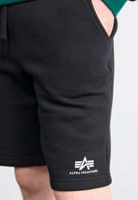 Shorts en coton noir avec une texture lisse et une taille élastique, ornés d'un logo blanc avec des rayures en angle sur l'ourlet inférieur.