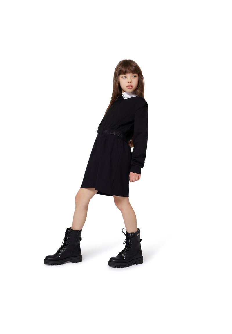 Svart langermet kjole med innsvingt midje og hvit krage. Kombinert med svarte snøresko med grov tekstur.