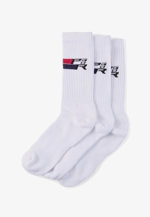 Kolme valkoista, poimutettua nilkkasukkaa, joissa on punainen, laivastonsininen ja musta logo lähellä yläosaa, asetettuna päällekkäin valkoisella taustalla.