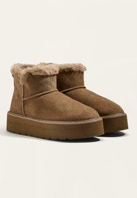 Stivaletti alla caviglia in suede marrone con morbida fodera in pelliccia, punta rotonda e suola platform spessa e testurizzata per un'altezza e comfort aggiuntivi.