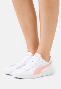Sneakers bianchi con accenti rosa, realizzati in materiale sintetico, caratterizzati da un design elegante, chiusura con lacci e suola in gomma testurizzata.