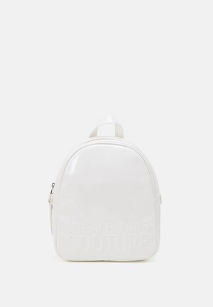 Lille hvid skinnende rygsæk med afrundet top, front lynlåslomme og præget "Versace Jeans Couture" logo på en glat overflade.