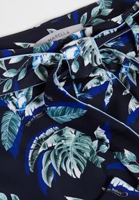 Marinfärgad tyg med tropiskt blad- och fågeltryck. Mjuk textur i nyanser av grönt och blått, med ljusblå accenter och en varumärkesetikett.