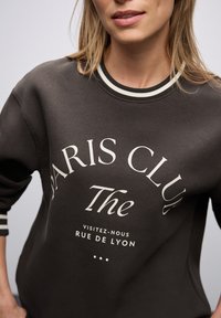 Ciemnoszara bluza z miękkiego materiału, z białym napisem "PARIS CLUB" oraz paskami na mankietach. Klasyczny okrągły dekolt.