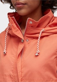 Korallfärgad jacka med dragkedja framtill, huva och justerbara dragsnören. Tillverkad av slät tyg med tryckknappdetaljer.