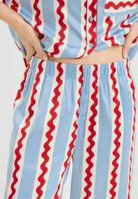 Blåt og hvidt sæt med pyjamas i striber med røde bølgede mønstre, knap-op skjorte med en lomme og bukser med elastik i taljen.