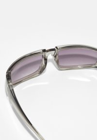 Sunglasses with a transparent gray frame and gradient purple lenses, featuring curved edges and a sleek, angular design.